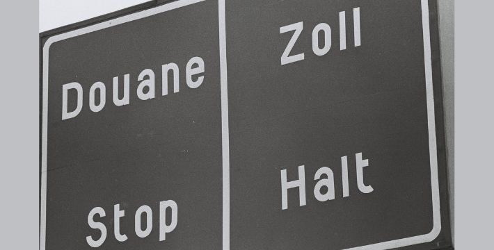 A bilingual road sign with Douane Stop in French on the left and Zoll Halt in German on the right, indicating a customs checkpoint. The sign has a black background with white text.