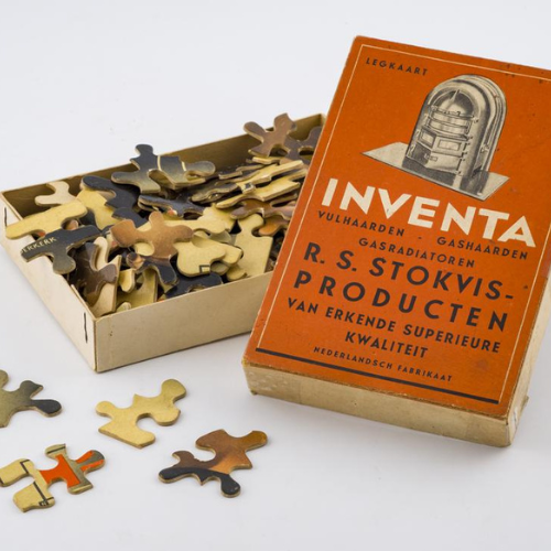 Vintage puzzle box with scattered pieces. The orange lid features an illustration of a heater, highlighting