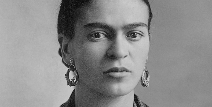Black and white photo of Frida Kahlo wearing earings, dark hair parted in the middle and tied back.