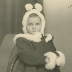 A little girl, wearing a winter coat trimmed with white leather and a hat,