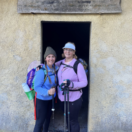 Two women hikers standing in the doorway of a historic building after a long hike.
